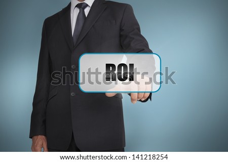 Businessman touching tag with roi written on it on blue background