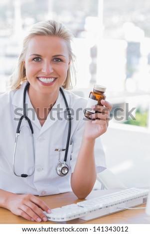Smiling nurse holding a medicine jar and typing on keyboard