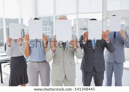 Buisness team holding up blank pages and covering their faces in the office