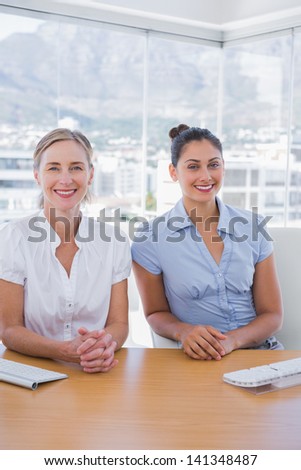 Happy businesswomen sitting side by side at desk in office