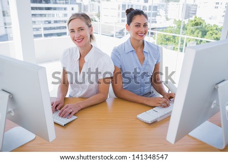 Smiling businesswomen working side by side at desk in office