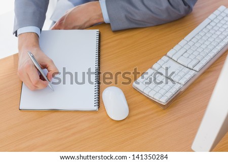 Businessman writing on blank notepad at his desk