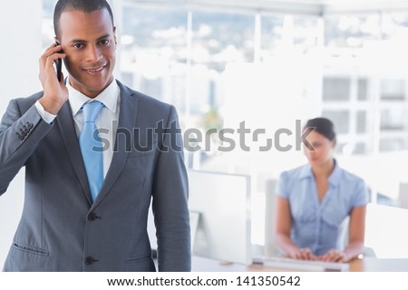 Happy businessman on a call with woman working at desk behind