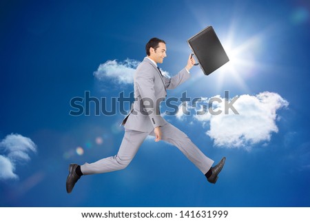 Happy businessman jumping with his briefcase in bright blue sky background