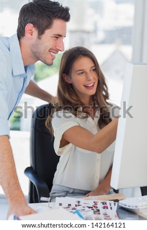 Two photo editors working together on a computer with contact sheets on the desk
