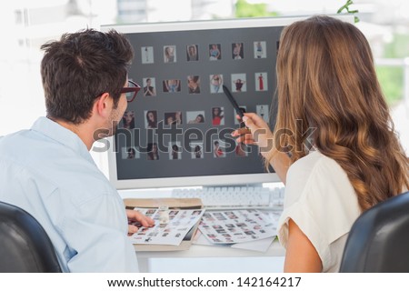 Photo editor pointing at computer while working on computer with a colleague