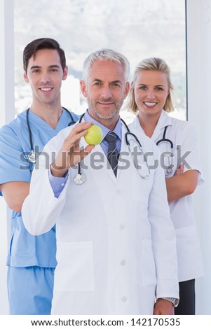 Cheerful medical staff standing together while one is holding a green apple