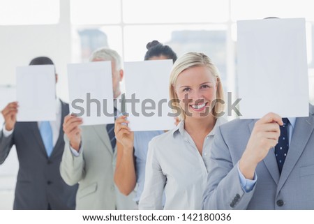 Business team covering face with white paper except for one woman smiling at camera