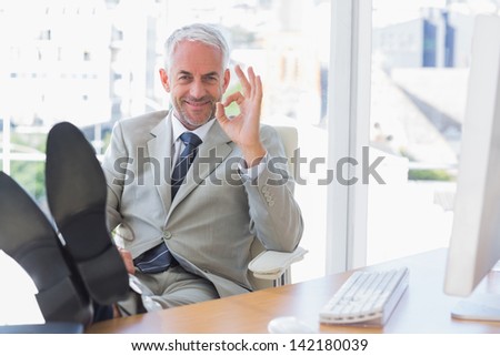 Happy businessman giving ok sign with feet up on his desk
