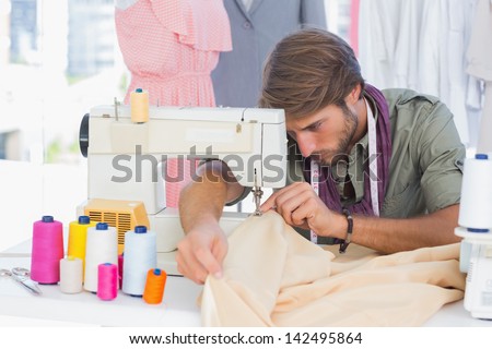 Handsome fashion designer sewing with a sewing machine