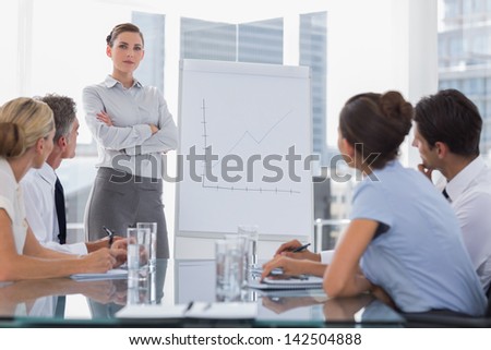 Businesswoman with arms folded in front of a growing chart during a meeting