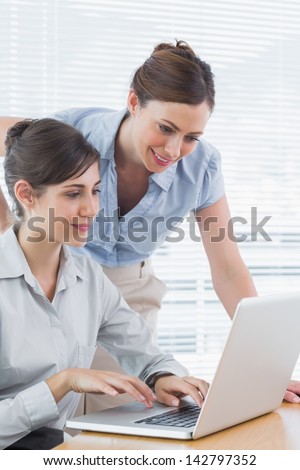 Businesswoman leaning over to look at colleagues laptop at desk in office