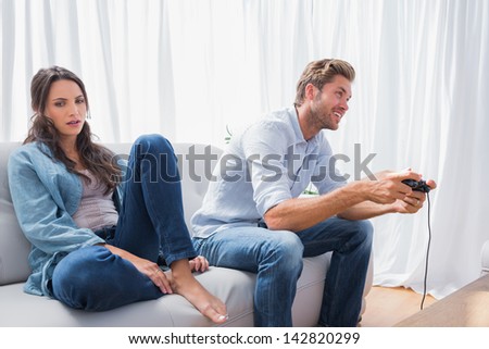 Man playing video games next to his annoyed partner sat on the couch