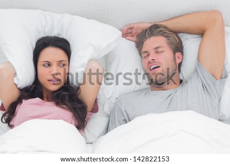 Pretty woman annoyed by the snoring of her husband in bed