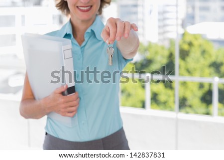 Estate agent showing house keys to camera in bright office