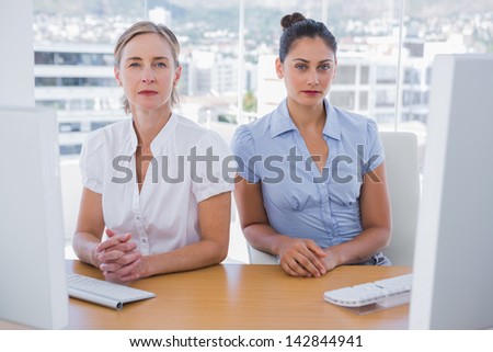 Serious businesswomen sitting side by side at a desk in the office