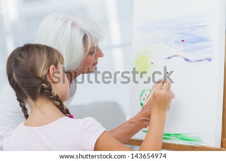 Grandmother teaching granddaughter how to paint at home