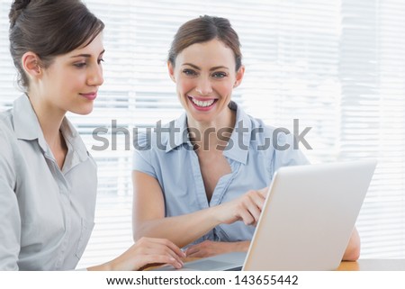 Two happy businesswomen working on laptop together at desk in office
