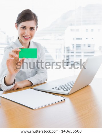 Pretty businesswoman showing green business card at her desk in office