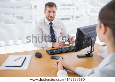 Businessman smiling at camera in his office with co worker at his desk