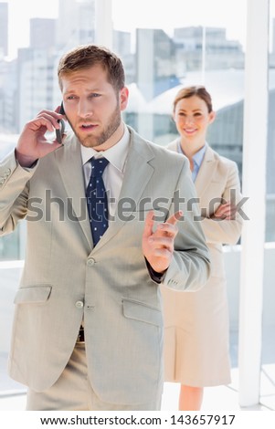 Businessman talking on phone with colleague standing behind him