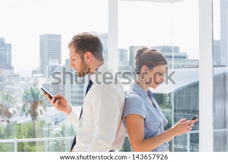 Business team standing back to back and texting in a bright office