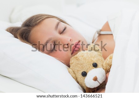 Cheerful girl sleeping with her teddy bear in her bed