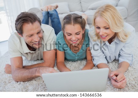 Happy parents and daughter using a laptop lying on a carpet