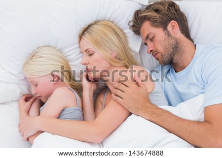Couple sleeping with cute daughter in bed