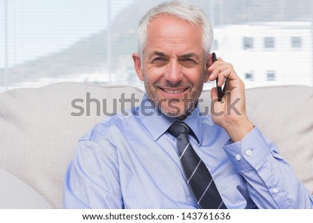 Businessman calling on smartphone and smiling at camera on sofa in staffroom