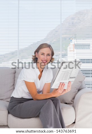 Businesswoman sitting on couch and holding newspaper in bright office