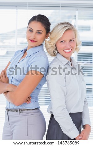 Attractive businesswomen with arms crossed standing back to back in a bright office