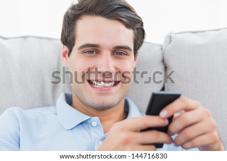 Portrait of a man text messaging with his phone sat on a couch