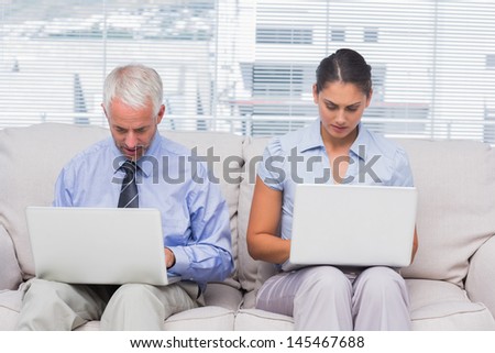 Business people sitting on sofa using their laptops in staffroom