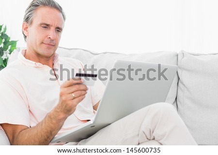 Man on his couch using laptop for online shopping at home in living room