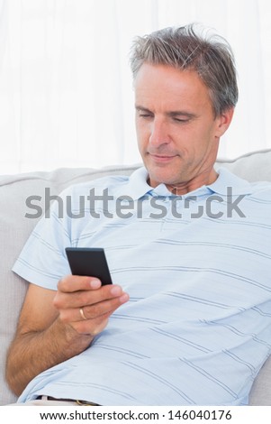 Man relaxing on his sofa sending a text on smartphone at home