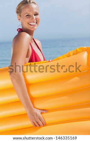 Smiling woman holding air mattress on beach
