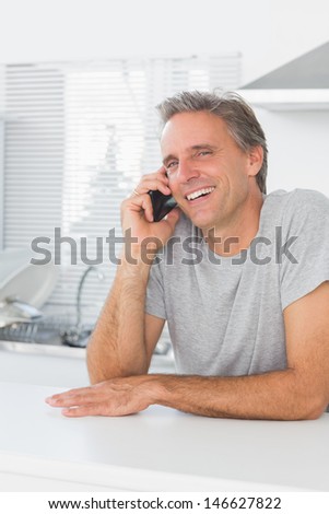 Laughing man making phone call in kitchen looking at camera