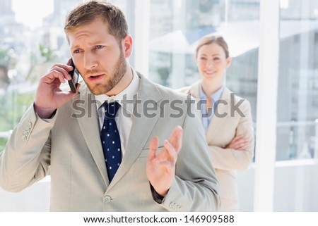 Businessman speaking on phone with colleague standing behind