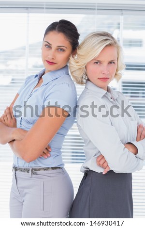 Serious businesswomen with arms folded standing back to back