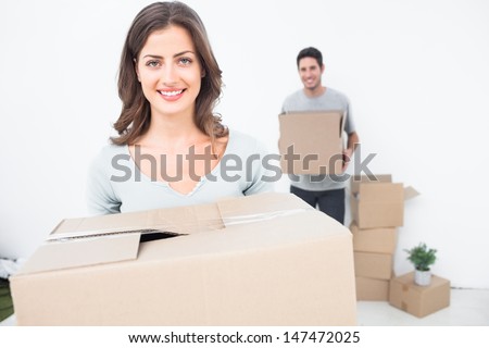 Pretty woman holding boxes in her new house with her husband on the background