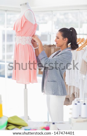 Attractive designer fixing dress on a mannequin in a studio