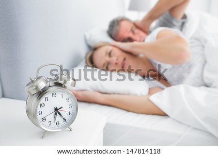 Couple covering their ears from alarm clock noise in bedroom at home