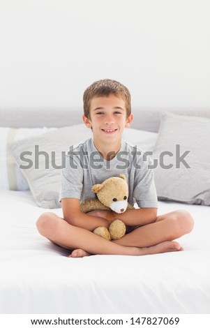 Little boy sitting on bed holding his teddy bear at home