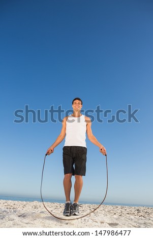 Cheerful sporty man jumping rope on the beach