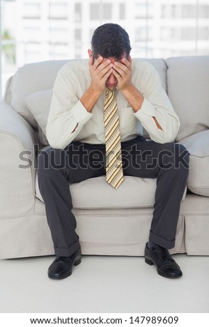Troubled businessman sitting on sofa in bright office