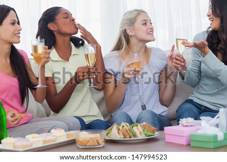 Friends drinking white wine and chatting during party at home on couch