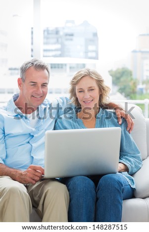 Smiling couple sitting on their couch using the laptop at home in the sitting room