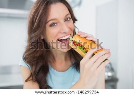 Cheerful brunette in her kitchen eating sandwich