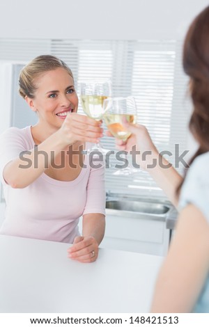 Radiant women having a toast with white wine in the kitchen